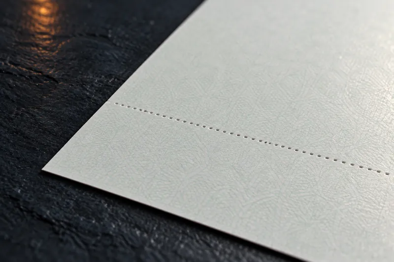 A macro view of the corner of a blank check safety stock sheet, its fine background pattern and perforation lit from the side.